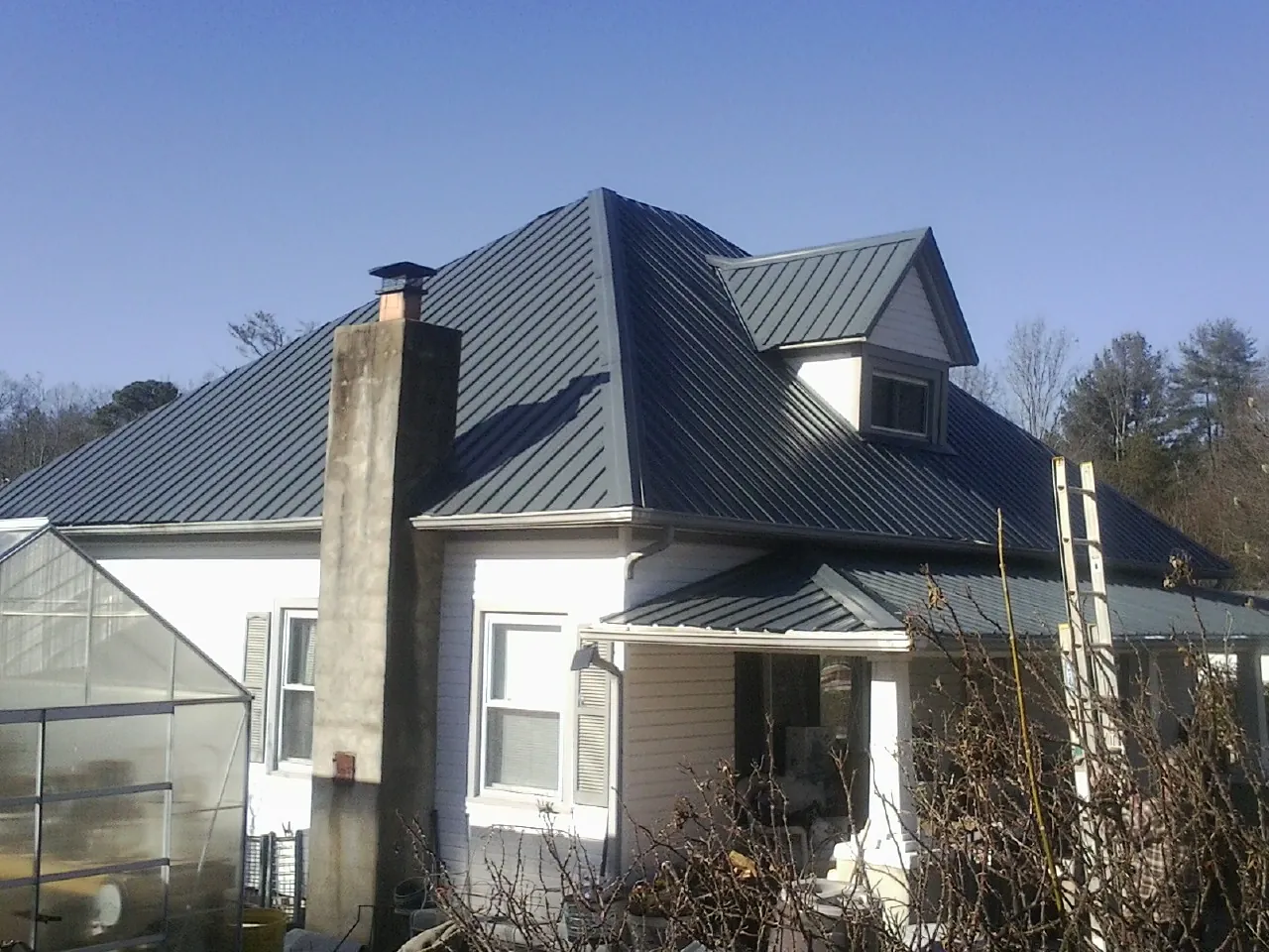 Dark blue standing seam metal roof on a white farmhouse with dormer — Slate & Tile Roof Repair by Roofing Brothers in Thurston