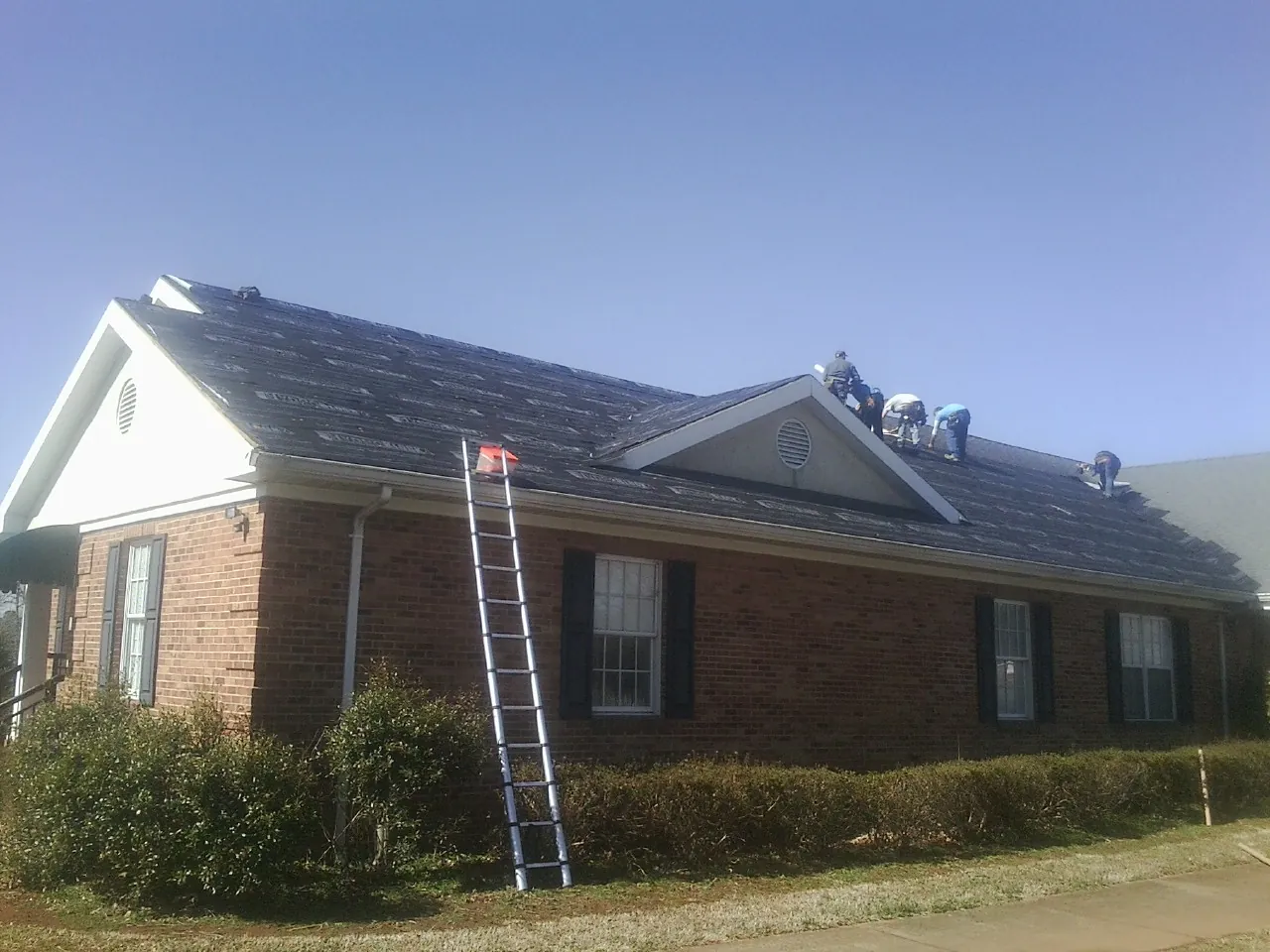 Crew tearing shingles off a brick ranch roof with a ladder set — Emergency Roof Repair work by our crew in Thurston