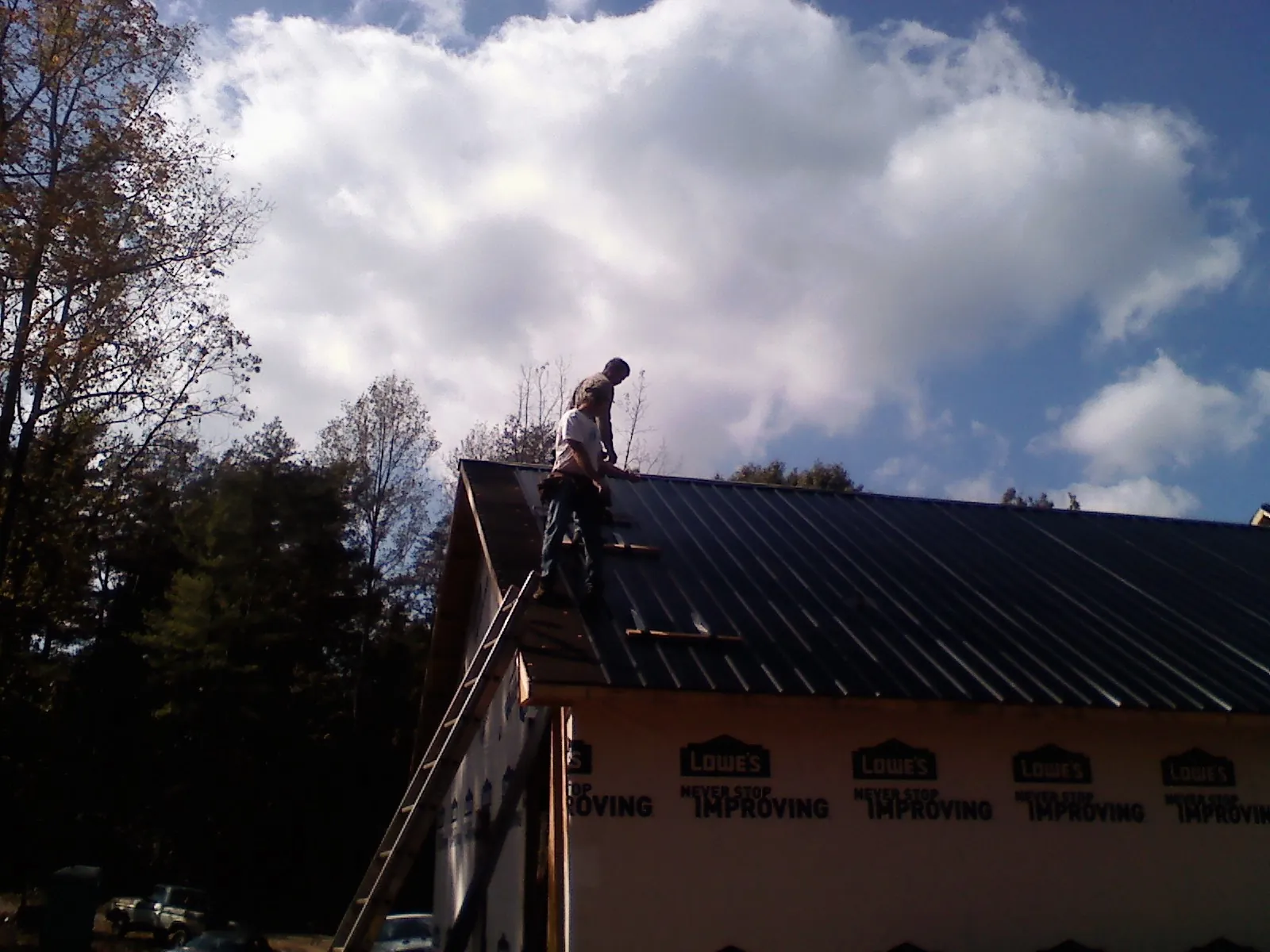 Roofer fastening dark metal panels high against a cloudy sky, from a Roof Inspection job in Thurston