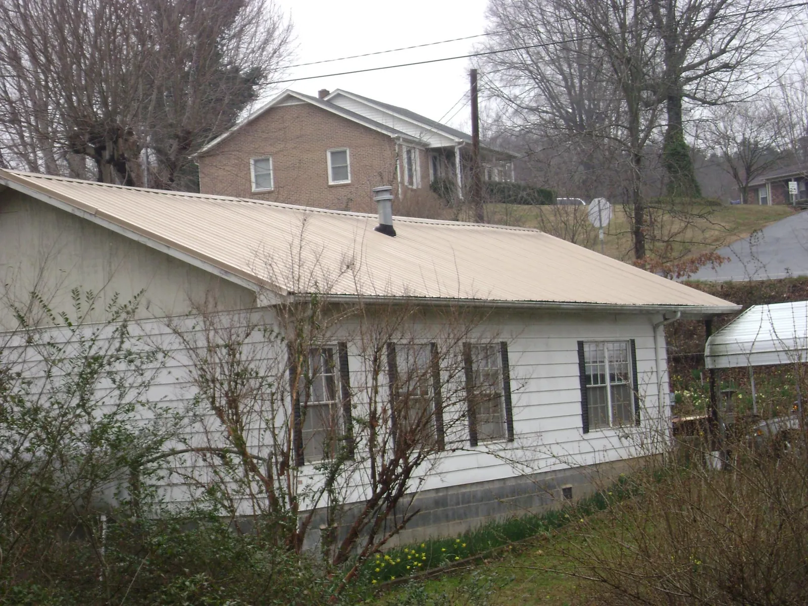Tan metal roof on a white sided house set into a hillside — Commercial Roofing by Roofing Brothers in Thurston